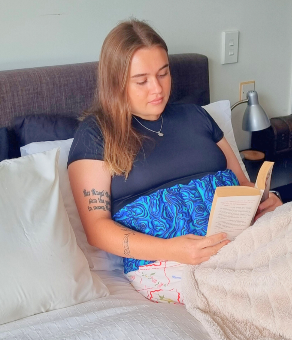 Lady_laying_in_bed_reading_abook_while_wearing_a_waist_wheat_bag_for_tummy_pain