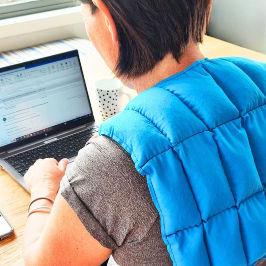 Lady wearing turquoise over shoulder wheat bag while working at her computer