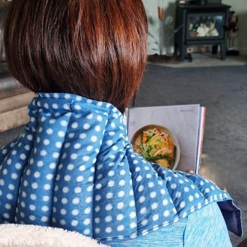 Lady sitting on the couch wearing a pennywise neck wheat bag while reading a magazine