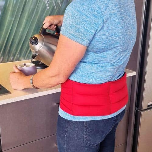 Lady in the kitchen wearing a red waist wheat bag and making herself a cuppa