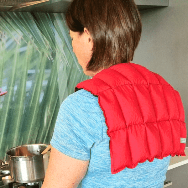 Lady wearing red shoulder wheat bag while cooking on the stove