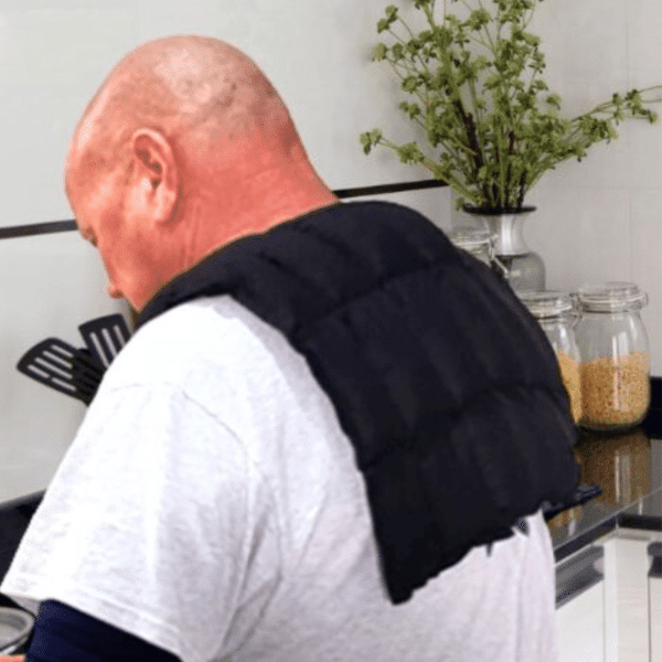Man wearing black over shoulder wheat bag while at the kitchen bench